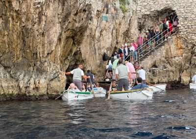 Visitors waiting on stone steps as rowboats collect passengers outside Capri’s Blue Grotto