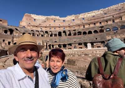 Mike and Jacquie taking a selfie inside the Colosseum, with ancient seating tiers behind them